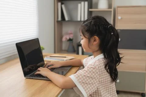 Young girl using laptop computer sitting at wooden desk in cozy home enviro.. Stock Photos