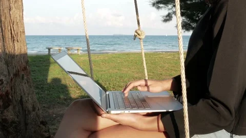 Young girl Using a Laptop next to a beach on a swing Stock Footage 239020008