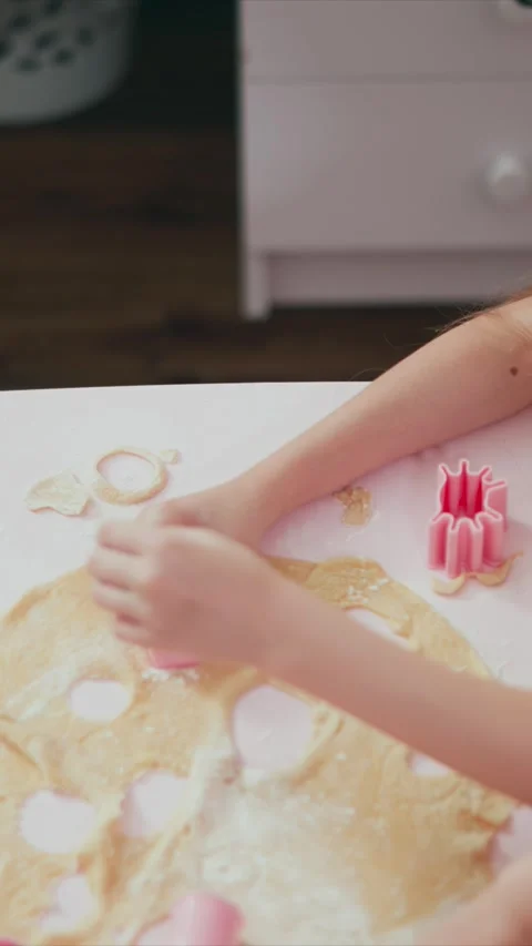 Young girl using pink cookie cutters to shape dough into heart and circular Stock Footage 345982960