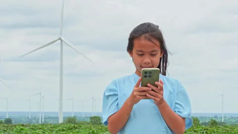 Young girl using smartphone in green field with wind turbine landscape backgroun Video stock 342912110
