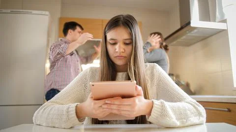 Young girl using tablet computer and ignoring arguing and shouting parents Stock Photos