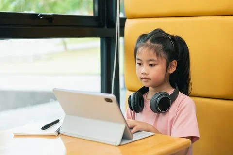 Young girl using tablet computer with headphones sitting at desk in bright .. Stock-Fotos