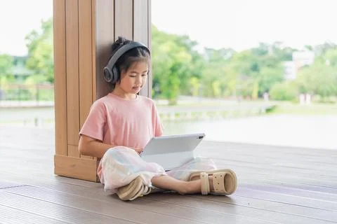 Young Girl Using Tablet Device While Sitting on Wooden Floor Near Large Win.. Stock Photos