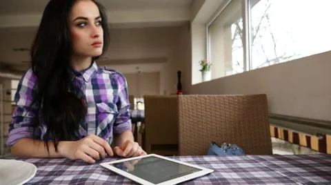 Young girl using tablet pc in the restaurant. She looks outside the window Stock Footage 61408550