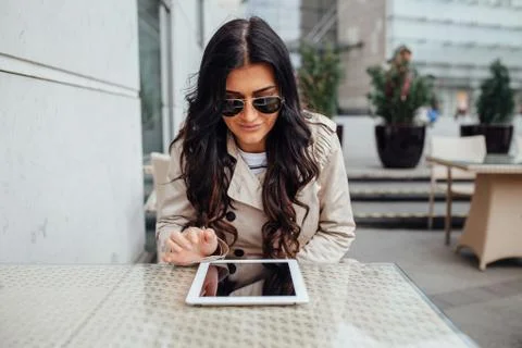 Young girl using tablet pc while sitting outside the cafe. Urban background. Stock Photos