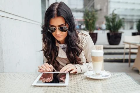 Young girl using tablet pc while sitting outside the cafe. Urban background. Stock Photos