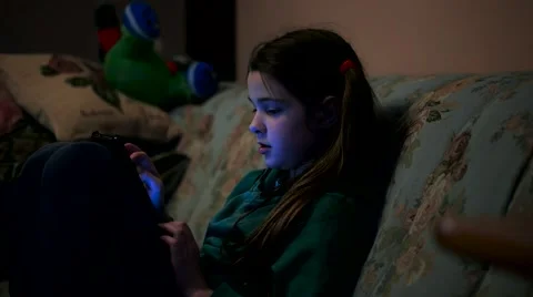 Young girl using a tablet sitting on a sofa in the darck room Stock Footage 60390118