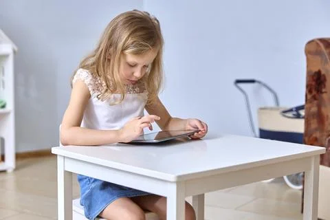 Young Girl Using Tablet at Table with Focused Expression Fotos Stock