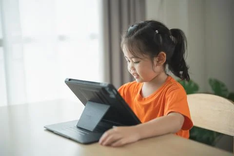 Young girl using tablet on table with sunlight streaming in through window,.. 库存照片