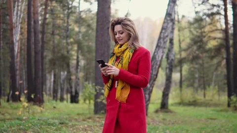 Young girl walking in autumn Park and texting a message on a mobile phone Stock Footage