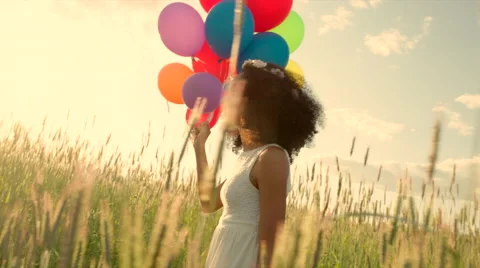 Young girl walking through a wheat field with colour balloons during sunset Stock Footage 64773633