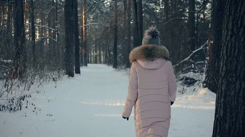 A young girl in a warm down jacket walks along the forest path in winter. HD Video stock 83533487