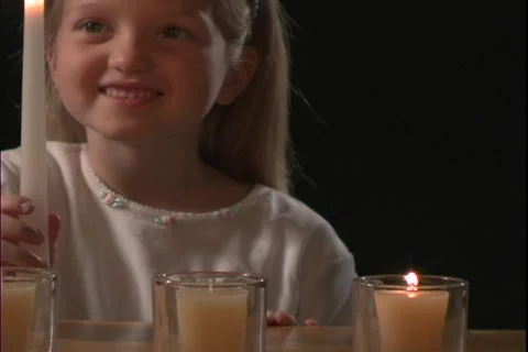 A young girl watches a flame of a candle. Stock Footage