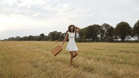 A young girl wearing a white dress with a straw hat and a suitcase. Straw and Stock Footage