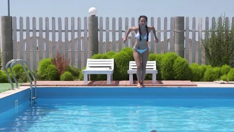 Four teenage girls in bikinis leaping into outdoor pool, Stock