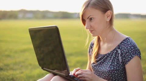 Young girl working on a laptop while sitting on a green lawn Stock Footage 52582837