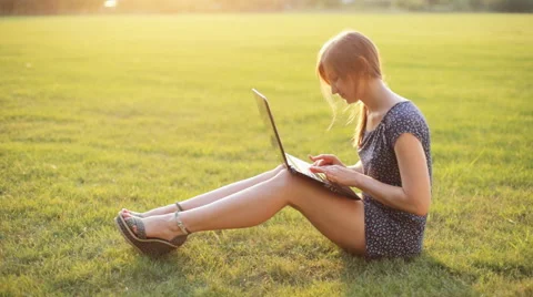 Young girl working on a laptop while sitting on a green lawn Stock Footage 52582997