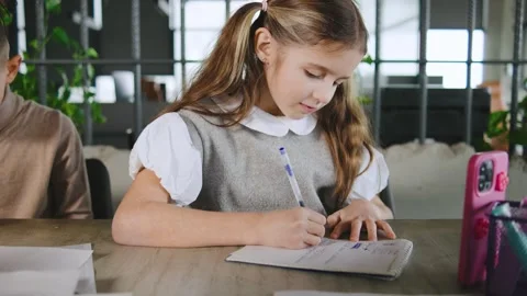 Young girl writes notes in a classroom while sitting at a table with others Stock Footage 331314635