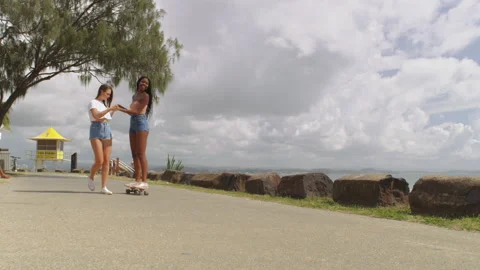 Young girls millennials learning how to skateboard at the beach with ocean in th Stock Footage 199459082