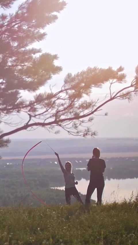 Young girls performing gymnastic elements with the tape on the hill under the Video stock 347203360