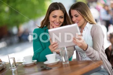 Young girls sitting at the cafe and reading gossip message. Stock Photos