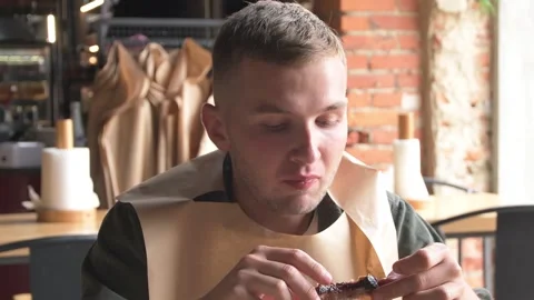 A young, good-looking guy is eating meat, nibbling on pork ribs at the table. Stock Footage 211427230