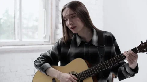Young good-looking guy with long hair plays acoustic guitar and sings Stock Footage 245615098