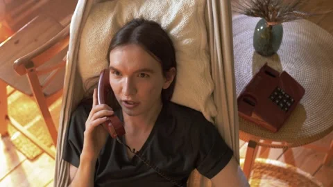 Young good-looking guy is lying in a hammock in an apartment talking Stock Footage 245991995