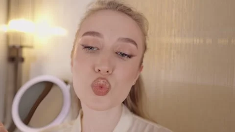 Young gorgeous female model applying red lipstick with a brush while looking in Stock Footage 328989601