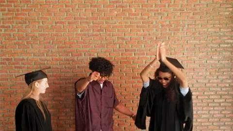 Young graduates dance joyfully in caps and gowns, celebrating their academic Stock Footage 326727082