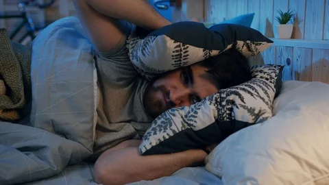 Young grumpy man trying to falling asleep. Noisy neighbors. Young man knocking Stock Footage 105656844