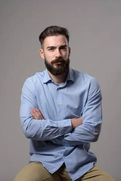 Young grumpy pessimistic bearded business man with crossed arms sitting and l Stock Photos