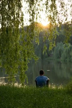 Young guy alone with thoughts on the lake. Concept: sunset, tranquility Stock Photos