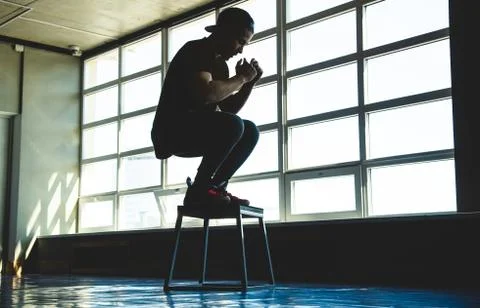 Young guy athlete is engaged in exercise and jumping in the gym. Silhouette Stock Photos