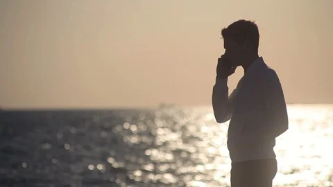 A young guy on the background of the sea at sunset finishes talking on the phone Stock Footage 113539108