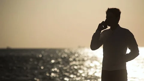Young guy on the background of the sea at sunset talking on the phone Stock Footage 113695806