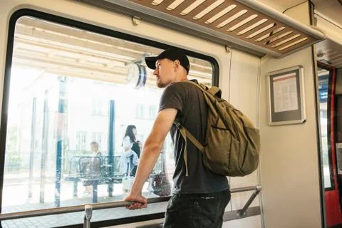 A young guy with a backpack inside the train looks out the window. Stock Photos