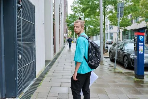 Young guy with backpack walking along street of modern city Stock Photos