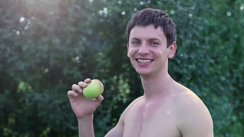 A young guy with a bare torso eating an apple in the garden Stock Footage 80895934