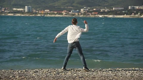 A young guy on the beach throws stones into the water Stock Footage 114165462