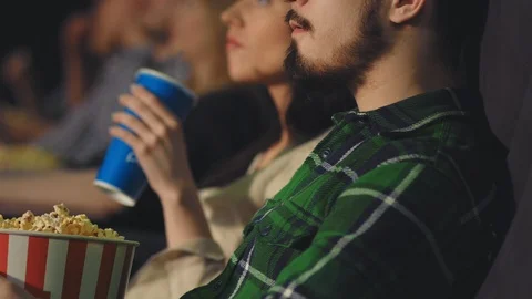 A young guy with a beard eats popcorn in the cinema Stock Footage 95502420