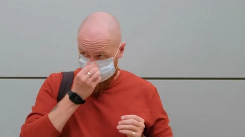 Young guy with a beard on the street puts on a medical mask on his face Stock Footage 139111725