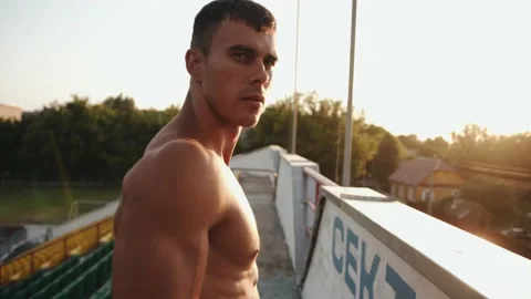 A young guy with big muscles stands at the city stadium at sunset and shows his Stock Footage 157183142