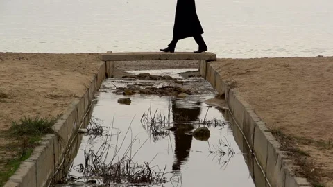 A young guy in a black coat crosses the river on a small bridge Stock Footage 274694611