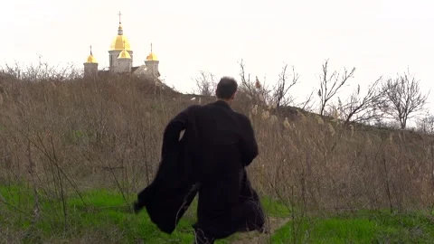 A young guy in a black coat runs against the background of a church Stock Footage 274695237