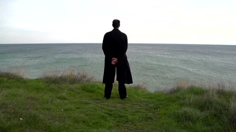 A young guy in a black coat stands on a cliff Stock Footage 274694698