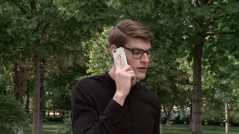 A young guy in black glasses goes and talks on the phone Stock Footage 79527673