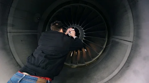 A young guy in a black jacket manually spins the blade of a passenger plane Stock Footage 102617589