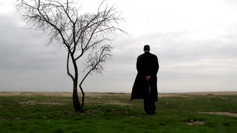 A young guy in a black long coat walk next to a tree Stock Footage 274694718