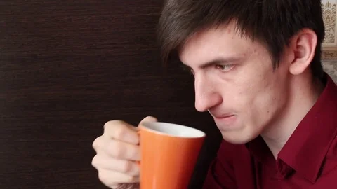 A young guy brings an orange mug to his mouth and makes a small sip Stock Footage 76900245